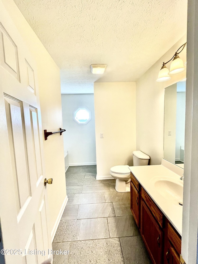 bathroom featuring vanity, toilet, baseboards, and a textured ceiling