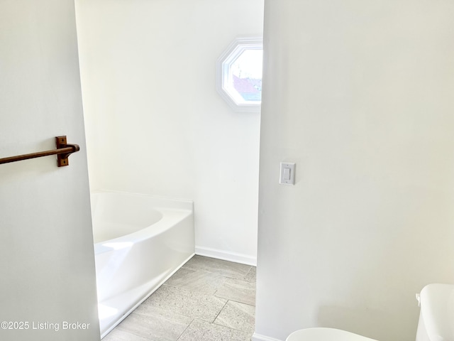 bathroom featuring a skylight, toilet, a bath, and baseboards