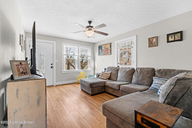 living area with baseboards, light wood-style floors, ceiling fan, and a textured ceiling