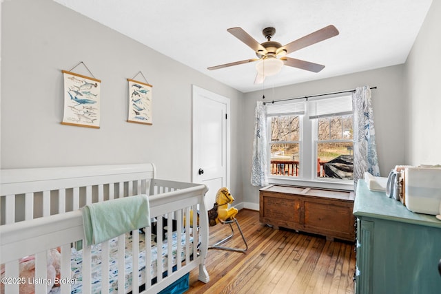 bedroom with baseboards, a crib, light wood-style floors, and a ceiling fan