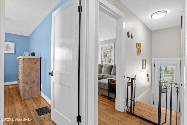 hallway with an upstairs landing, visible vents, light wood finished floors, and a textured ceiling