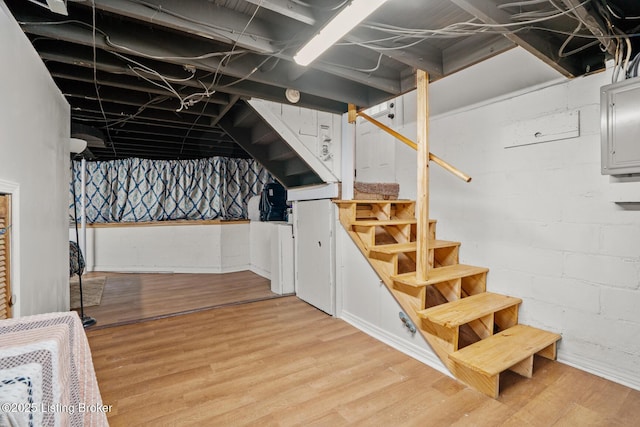 unfinished basement featuring concrete block wall, stairway, electric panel, and light wood finished floors