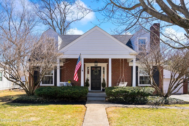 view of front of house featuring brick siding, covered porch, a chimney, and a front yard