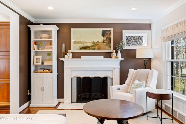 living area with a fireplace with flush hearth, visible vents, a wealth of natural light, and ornamental molding