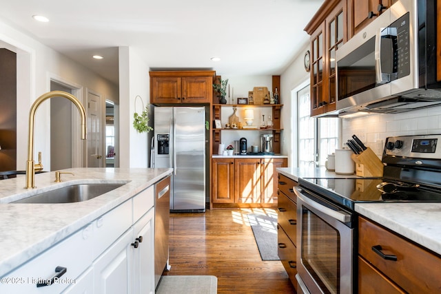 kitchen featuring a sink, backsplash, wood finished floors, stainless steel appliances, and open shelves