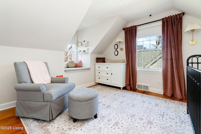 living area with lofted ceiling, wood finished floors, visible vents, and baseboards