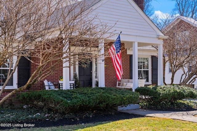 view of front of home featuring brick siding, covered porch, and a chimney