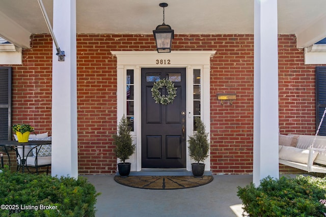 doorway to property featuring brick siding and covered porch