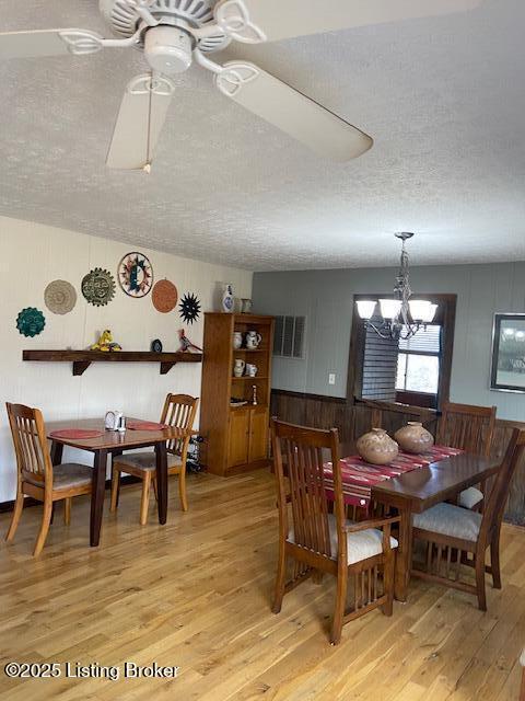 dining space with light wood-style flooring, ceiling fan with notable chandelier, and a textured ceiling