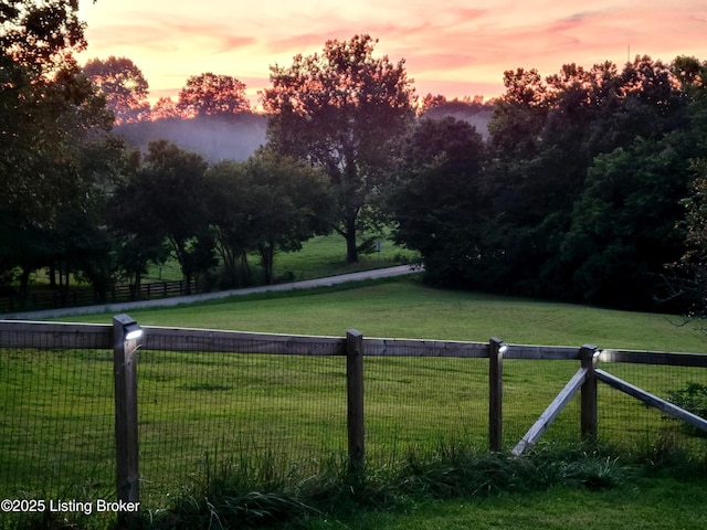 yard at dusk featuring a rural view and fence