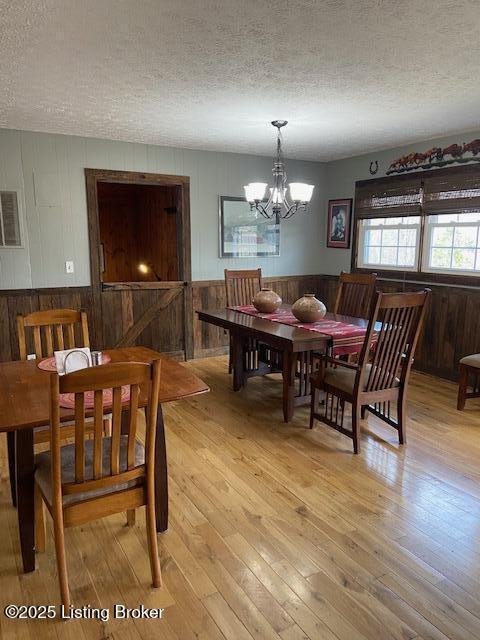 dining area with wainscoting, light wood-type flooring, a chandelier, and a textured ceiling