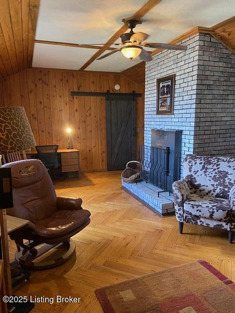 interior space featuring ceiling fan, vaulted ceiling, wood walls, a barn door, and a brick fireplace