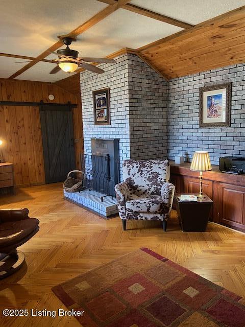 living room featuring vaulted ceiling, wooden walls, a barn door, and ceiling fan