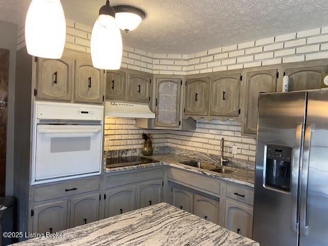 kitchen with oven, stainless steel refrigerator with ice dispenser, under cabinet range hood, a sink, and black electric cooktop