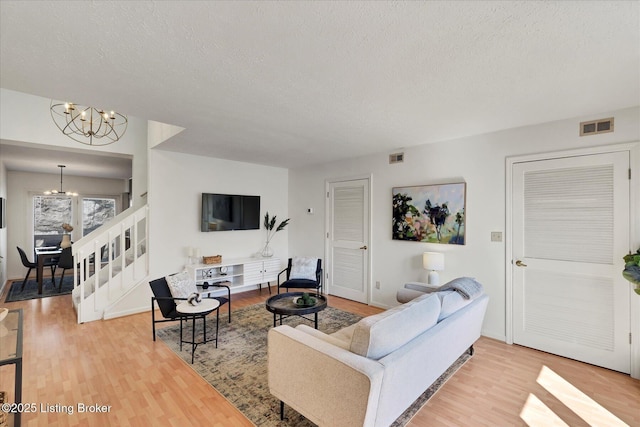 living room featuring a notable chandelier, visible vents, a textured ceiling, and wood finished floors