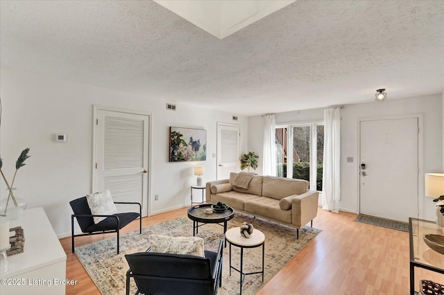 living room with light wood-type flooring, baseboards, a textured ceiling, and visible vents