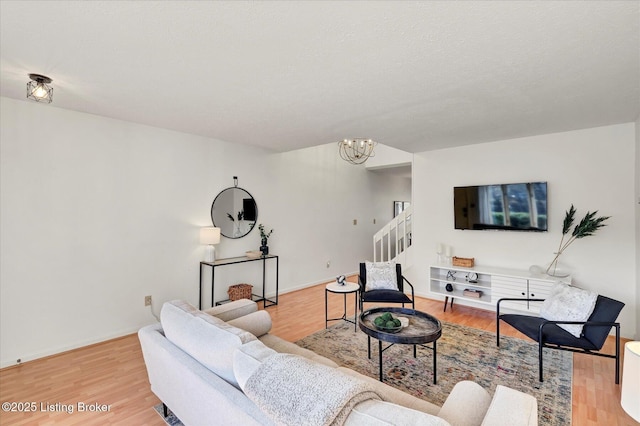 living area featuring stairs, light wood-style flooring, baseboards, and a chandelier