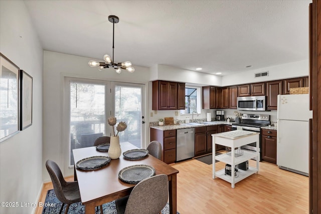 kitchen with visible vents, a sink, appliances with stainless steel finishes, light wood finished floors, and a chandelier