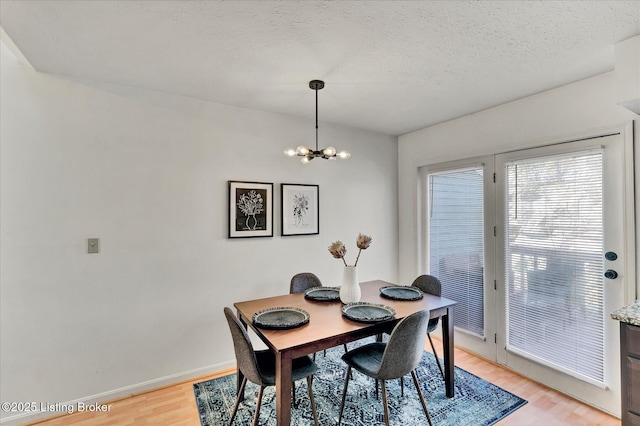 dining space featuring light wood-style floors, baseboards, a notable chandelier, and a textured ceiling