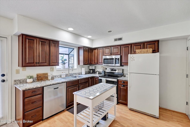 kitchen with visible vents, light wood-type flooring, light stone counters, stainless steel appliances, and a sink