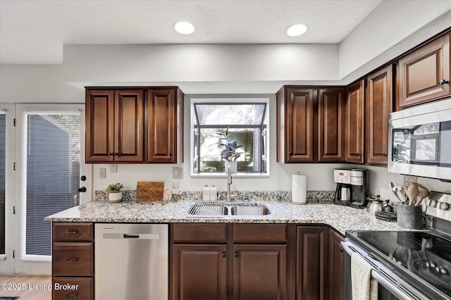 kitchen with light stone counters, a sink, dark brown cabinets, appliances with stainless steel finishes, and a textured ceiling