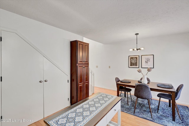 dining room with baseboards, an inviting chandelier, a textured ceiling, and light wood-style floors