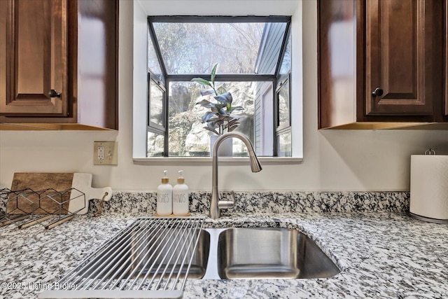 room details with a sink, light stone countertops, and dark brown cabinets