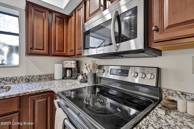 kitchen with light stone counters, brown cabinets, and stainless steel appliances