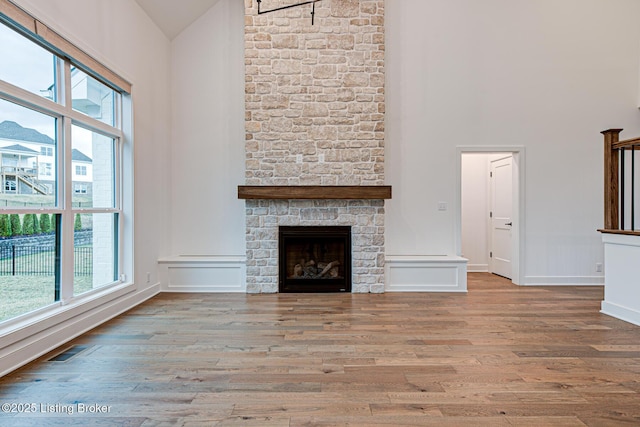 unfurnished living room with wood finished floors, visible vents, high vaulted ceiling, a fireplace, and a wealth of natural light