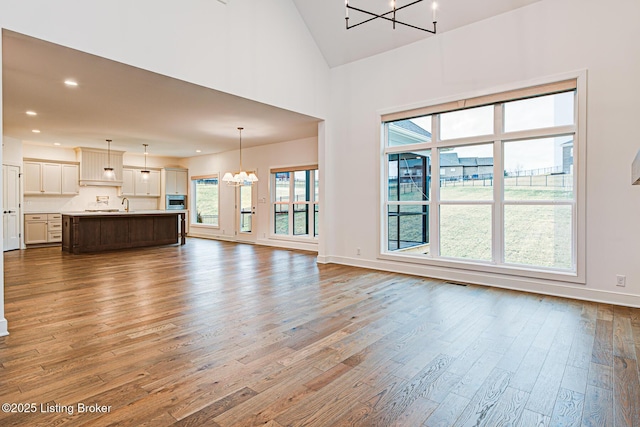 unfurnished living room with wood finished floors, baseboards, high vaulted ceiling, recessed lighting, and a notable chandelier