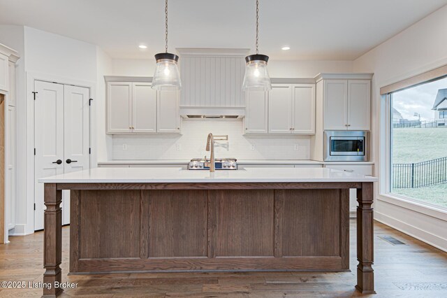 kitchen featuring tasteful backsplash, visible vents, light countertops, an island with sink, and stainless steel appliances