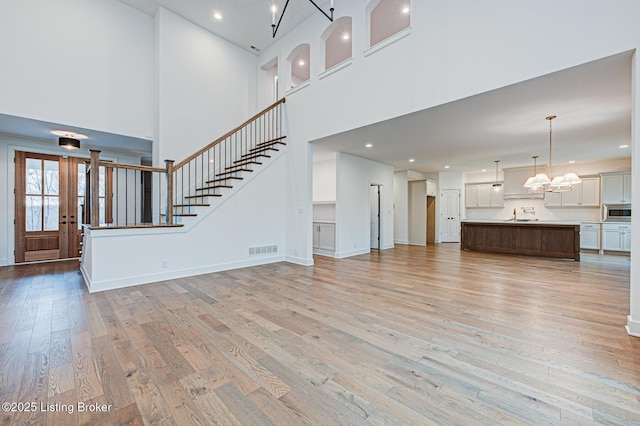 unfurnished living room with visible vents, a notable chandelier, stairway, light wood finished floors, and baseboards