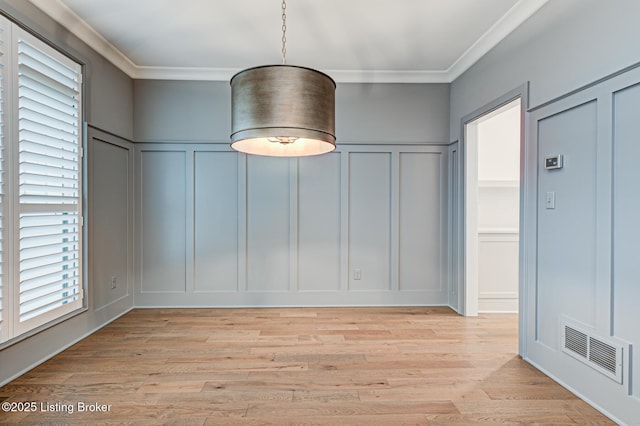 unfurnished dining area with light wood-type flooring, visible vents, crown molding, and a decorative wall