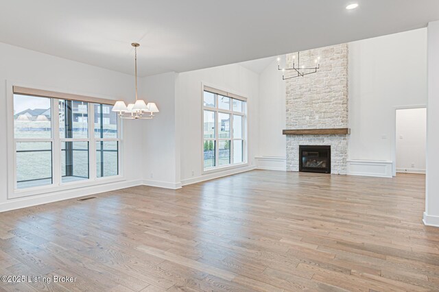 unfurnished living room featuring light wood finished floors, visible vents, baseboards, a fireplace, and a notable chandelier