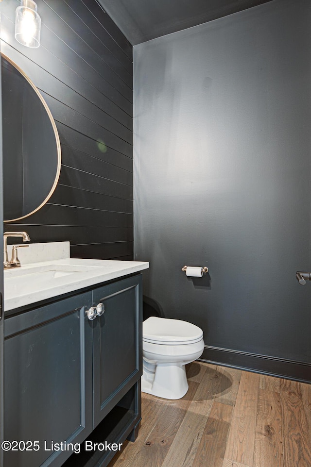 bathroom featuring baseboards, wood walls, toilet, wood finished floors, and vanity