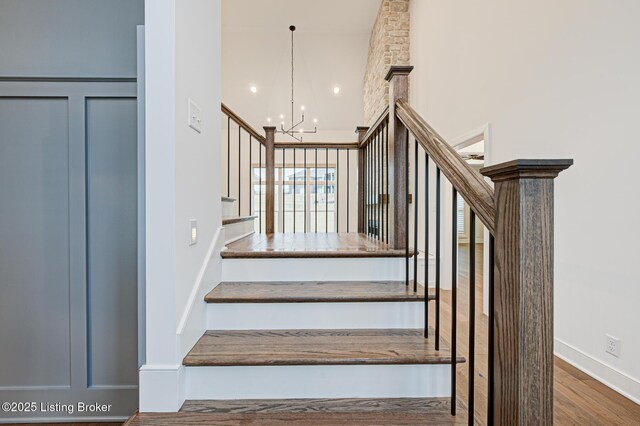 staircase featuring a chandelier, a towering ceiling, and wood finished floors