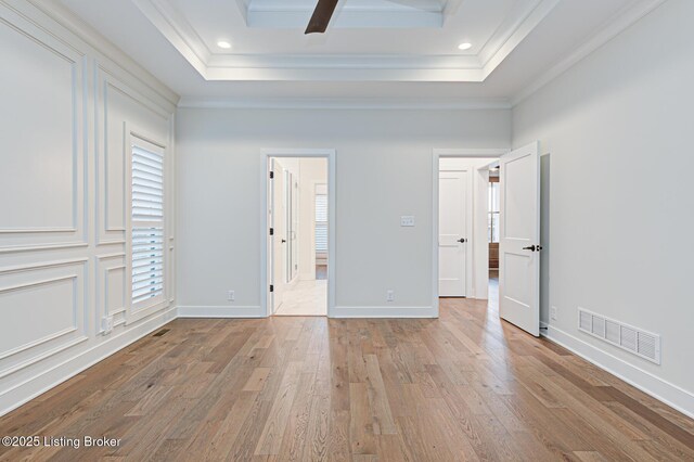 unfurnished bedroom with visible vents, a raised ceiling, baseboards, and wood finished floors