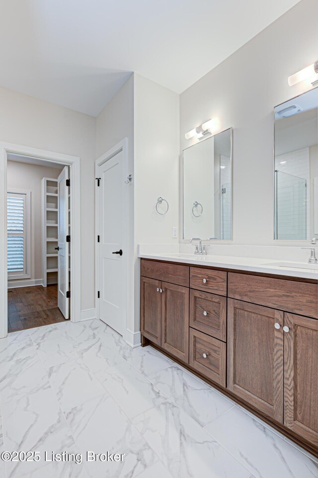 bathroom featuring double vanity, marble finish floor, a spacious closet, and a sink