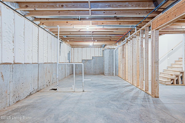 unfinished basement featuring electric panel and stairs