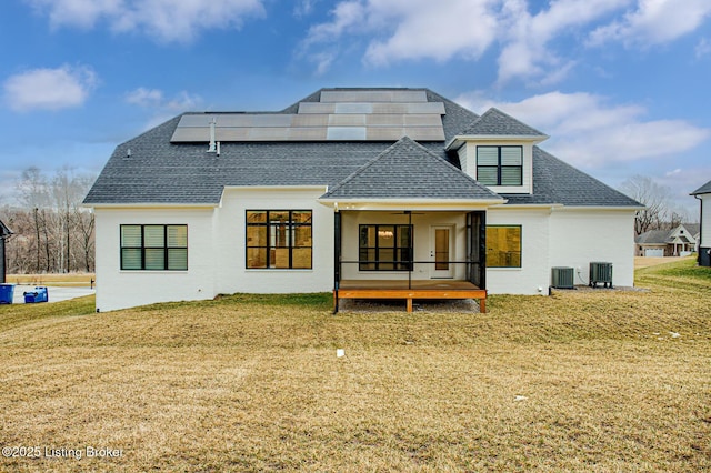 back of house featuring a yard, roof mounted solar panels, roof with shingles, and central AC