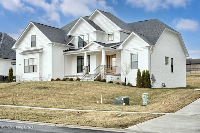 view of front of house with brick siding, roof with shingles, covered porch, and a front lawn