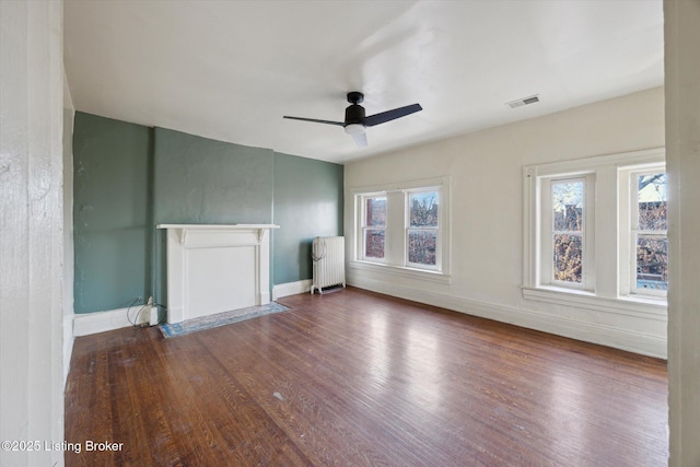 unfurnished living room featuring visible vents, a ceiling fan, wood finished floors, radiator heating unit, and baseboards