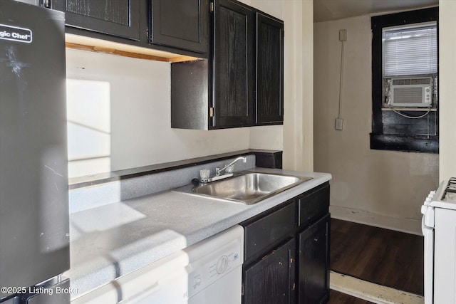 kitchen with a sink, wood finished floors, white appliances, light countertops, and dark cabinets