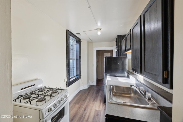 kitchen featuring dark cabinetry, wood finished floors, visible vents, white gas stove, and a sink