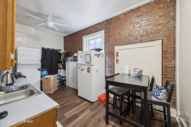 kitchen featuring brick wall, stacked washing maching and dryer, dark wood finished floors, freestanding refrigerator, and ceiling fan