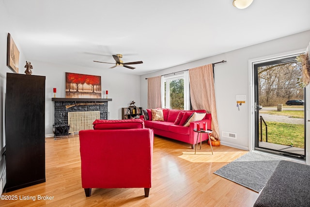 living room with wood finished floors, visible vents, baseboards, ceiling fan, and a stone fireplace