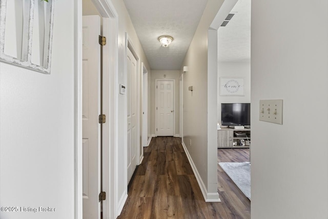 corridor featuring visible vents, dark wood-style floors, baseboards, and a textured ceiling