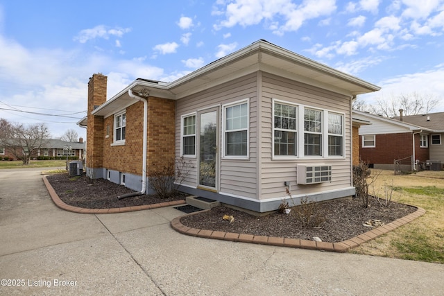 view of side of home featuring brick siding, driveway, a chimney, and central AC