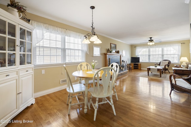 dining room featuring visible vents, a fireplace with raised hearth, light wood-style floors, crown molding, and baseboards