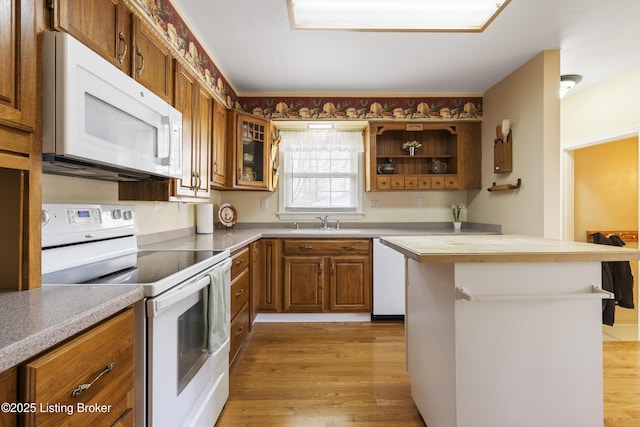 kitchen featuring a sink, white appliances, brown cabinetry, light wood finished floors, and glass insert cabinets